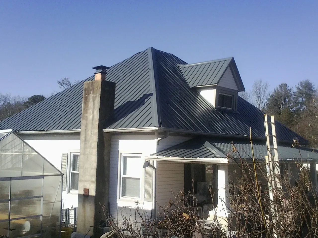 Dark blue standing seam metal roof on a white farmhouse with dormer — Slate & Tile Roof Repair by Roofing Brothers in Castile