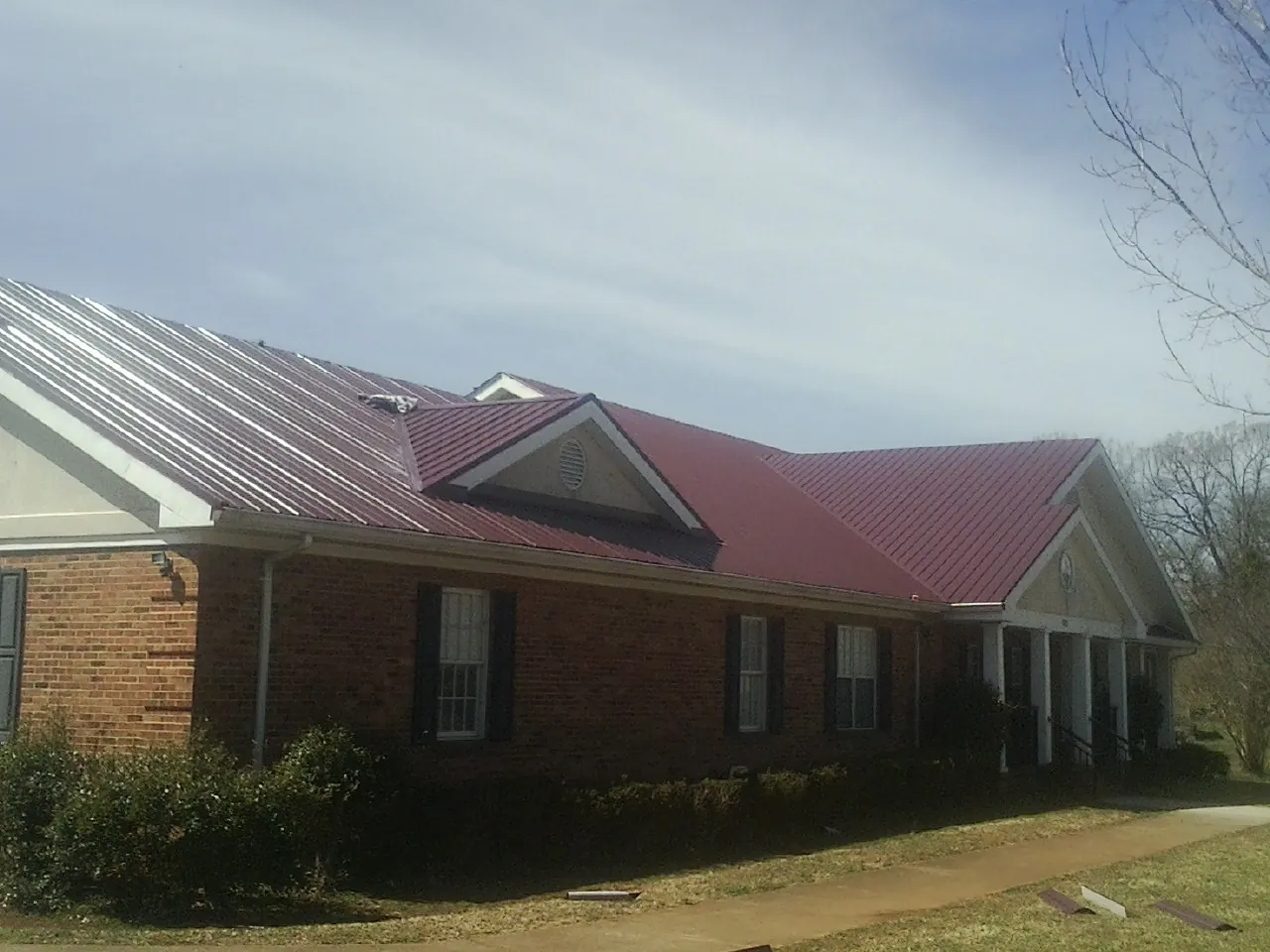 Red metal roof with gabled entries on a long brick building, from a Hail Damage Roof Repair job in Castile