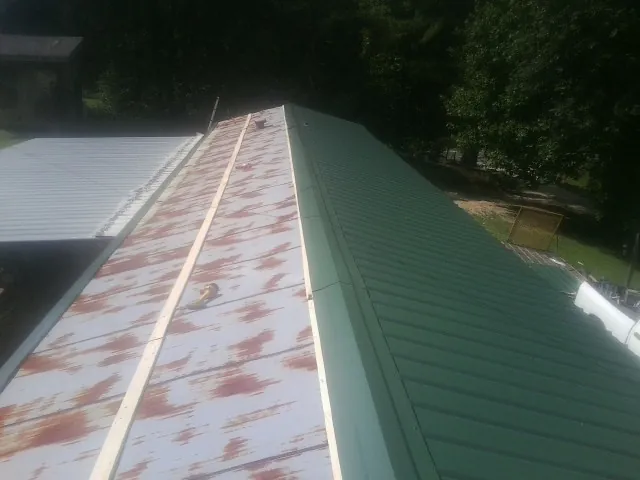 Old rusted panels beside newly installed green metal roofing — Wind Damage Roof Repair by Roofing Brothers in Castile