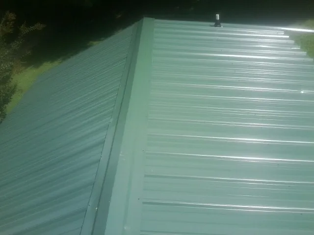 New green metal panels meeting at the ridge of a roof — Flat Roof Repair work by our crew in Castile