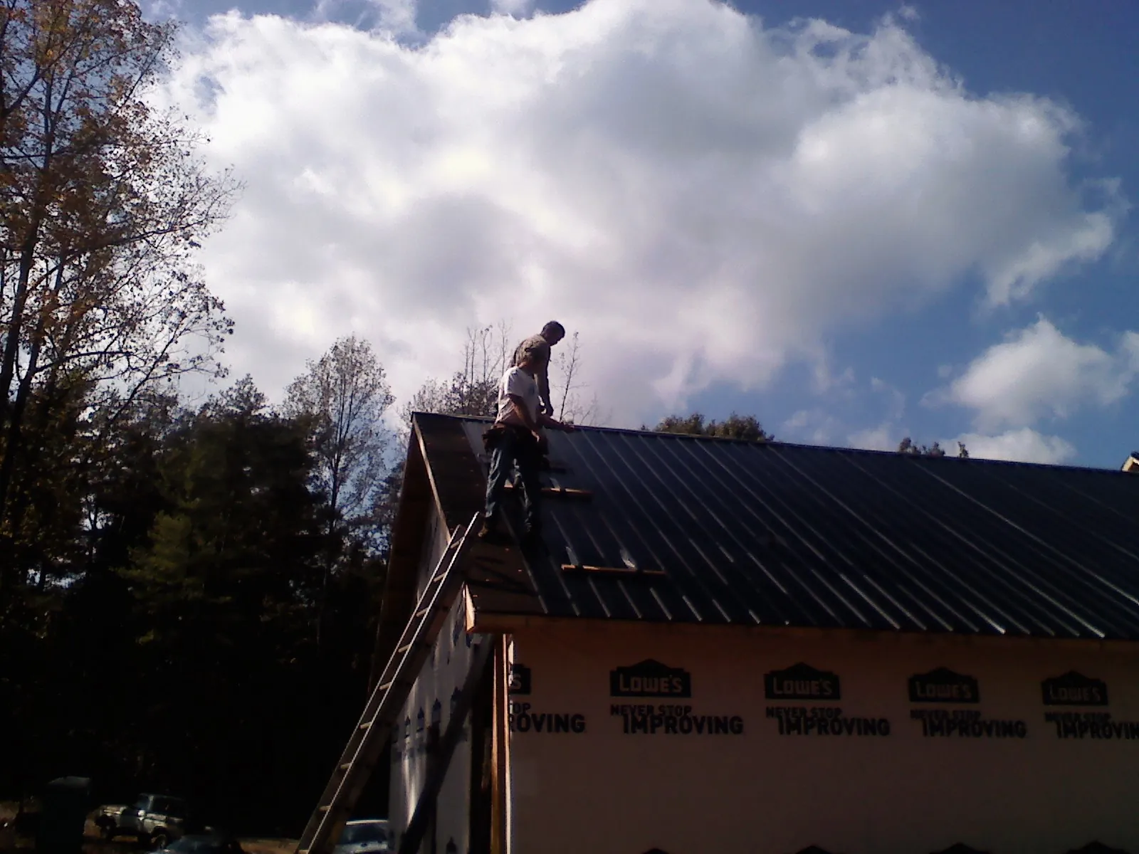 Roofer fastening dark metal panels high against a cloudy sky, from a Roof Inspection job in Castile