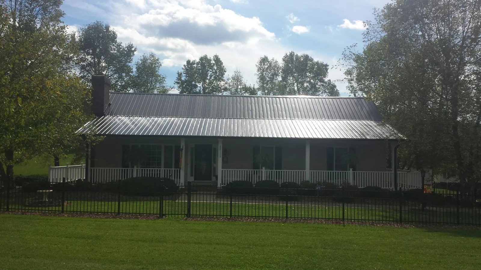 Gray metal roof on a brick ranch with a full width front porch — Gutter Guard Installation work by our crew in Castile