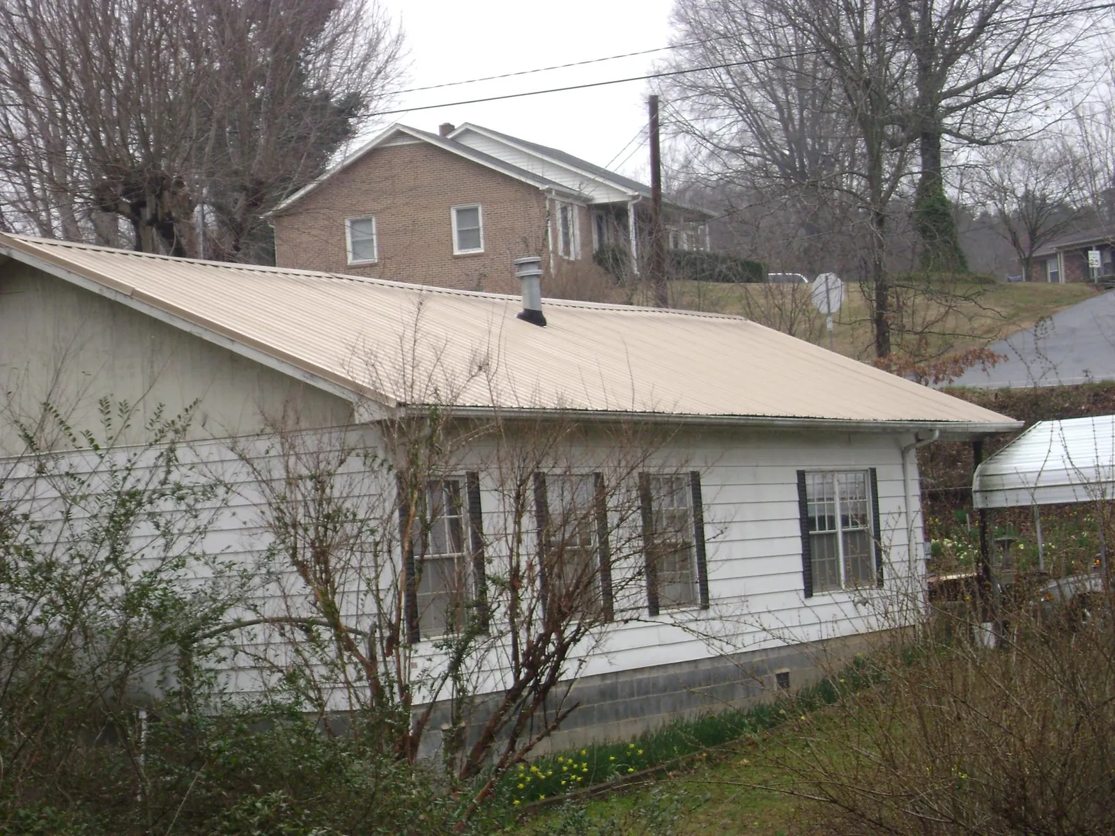 Tan metal roof on a white sided house set into a hillside — Commercial Roofing by Roofing Brothers in Castile