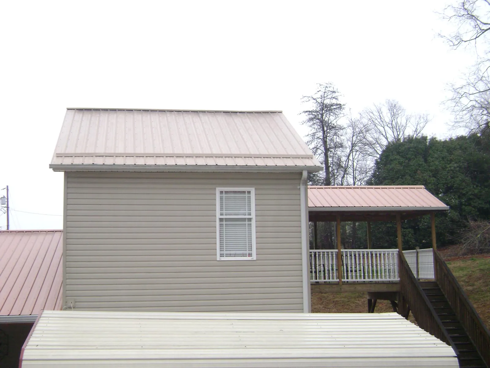 Tan metal roofs on a two story addition and attached porch, from a Roof Replacement job in Castile